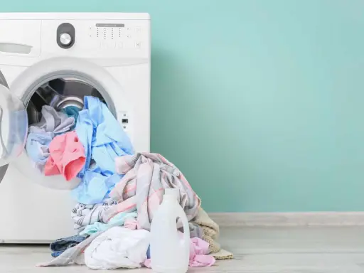Lavadora blanca con ropa de colores y botella de detergente. Aprende como limpiar la lavadora para un mejor lavado.