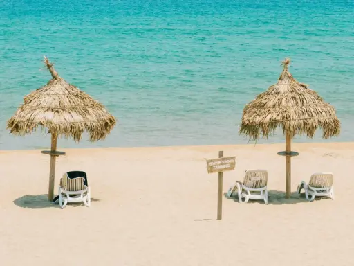Idealna pogoda Tunezja wrzesień: dwa słomiane parasole i leżaki na piaszczystej plaży, turkusowe morze w tle.