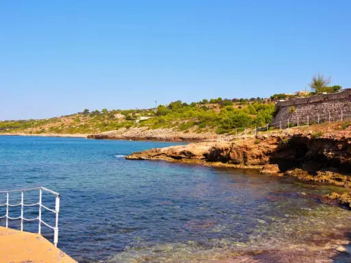 Scogliera rocciosa e mare cristallino a San Gregorio al mare, con vegetazione mediterranea e un muretto in pietra.