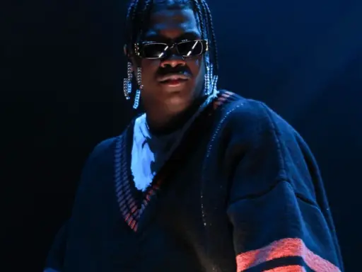 Lil Yachty w okularach i długich kolczykach, w swetrze z pomarańczowymi pasami. Let's start here.