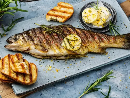 Perfekt gegrillte Forelle mit Kräutern, Zitronenscheibe und geröstetem Brot. Ein Genuss für jeden Fischliebhaber.