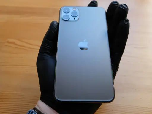 Ręka w czarnej rękawiczce trzyma elegancki iPhone 11 czarny. Obok leży czarne pudełko.