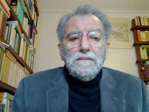 Uomo anziano con barba grigia, occhiali e giacca, circondato da scaffali pieni di libri. Il suo sguardo intenso suggerisce che ei fu significato.