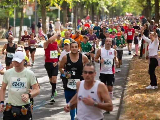 Läufer im Pulk auf einer Straße, einige mit Startnummern, die auf einen Marathon unter 4 Stunden hindeuten.