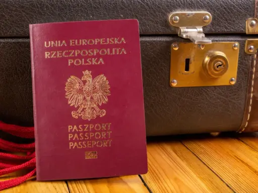 Polski paszport i brązowa walizka na drewnianym tle.