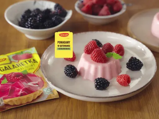 Panna cotta z malinami i jeżynami, obok opakowanie galaretki malinowej.