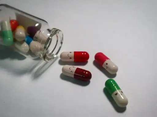 Kolorowe kapsułki, niektóre z uśmiechniętymi buźkami, wypadają z butelki. To mogą być psychotropy, które pomagają w trudnych chwilach.