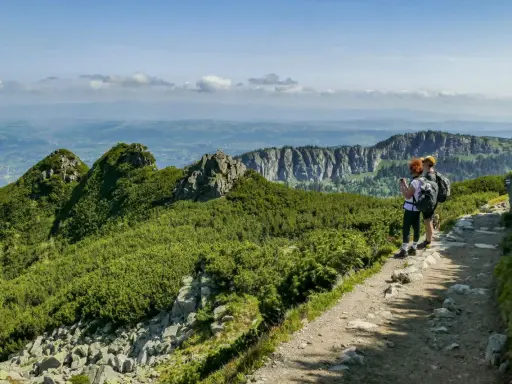 Dwie osoby z plecakami podziwiają widok na Tatry. Szlak jest kamienisty, ale stanowi łatwe zejście z Kasprowego Wierchu.
