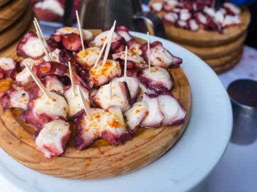 Pulpo a la gallega servido en tabla de madera, con palillos y espolvoreado con pimentón.