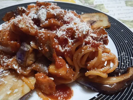 Un piatto invitante di pasta alla norma con melanzane fritte, sugo di pomodoro e ricotta salata grattugiata.