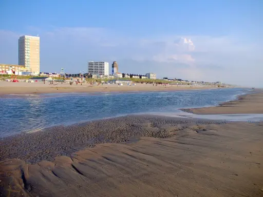 Piękny dzień nad morzem w Holandii. Piaszczysta plaża, spokojna woda i nowoczesne budynki w tle tworzą malowniczy krajobraz.