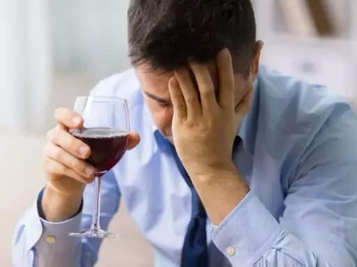 Hombre con copa de vino tinto, con la mano en la frente, buscando alivio en un vino sin histamina.