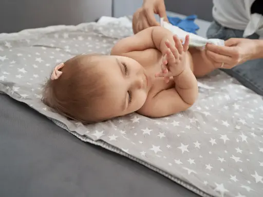 Bebé acostado en una manta con estrellas, mientras le cambian el pañal. Un paso más para dejar el pañal.