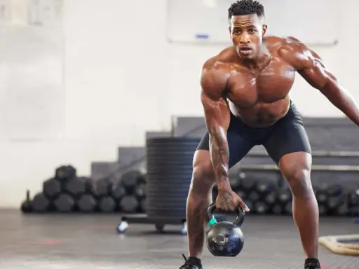 Ein Mann mit starkem Muskelaufbau hebt eine Kettlebell. Seine Anstrengung spiegelt die Ergebnisse von intensiven Trainingseinheiten wider, wie sie in Studien zum Muskelaufbau untersucht werden.