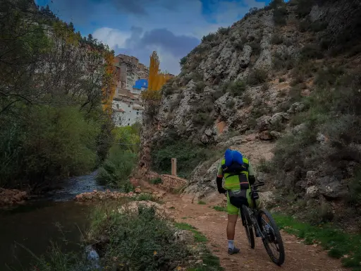 Ciclista en la ruta de las esculturas Bogarra, junto a un río y un pueblo en la ladera.