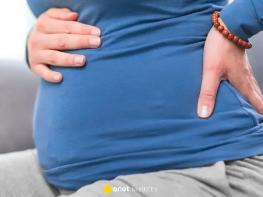 Ciężarna kobieta trzyma się za brzuch i plecy, odczuwając dyskomfort. To może być objaw biegunki przed porodem.
