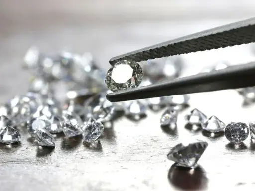 Un diamante etico, scintillante, tenuto da una pinzetta, circondato da altri brillanti su una superficie metallica.
