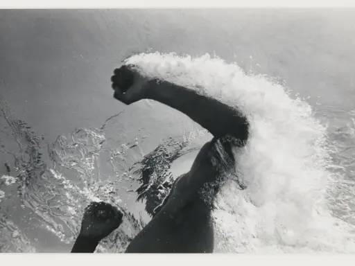 Underwater shot of a swimmer's arms and torso, creating a dramatic splash. The image captures the power and motion of a flip schulke.