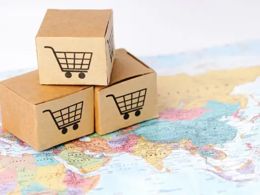 Trzy kartony z ikonami koszyków na zakupy na mapie świata. Symbolizują handel transgraniczny i globalny e-commerce.