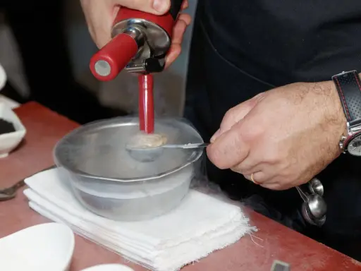 Chef usa sifón para crear texturas aireadas, ideal para recetas de espumas para sifón. Humo frío rodea el bol.