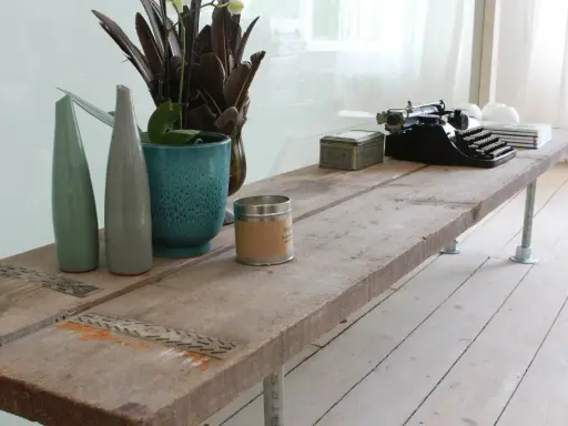 Une table basse rustique, idéale pour savoir que faire avec des vieilles planches de bois. Elle est décorée d'une machine à écrire, de vases et d'une bougie.