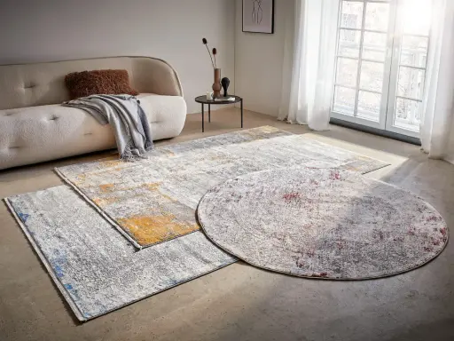 Mattor inspiration: En rund och två rektangulära mattor med abstrakt mönster i grått, vitt, gult och rött ligger på ett betonggolv framför en soffa.