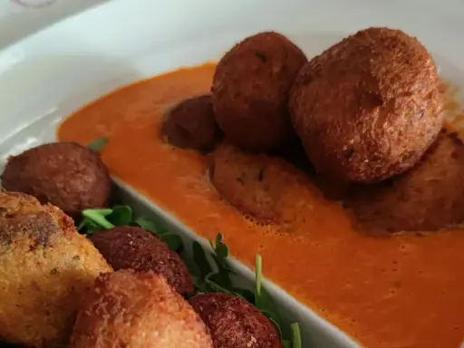 Polpette di pane dorate e croccanti, servite su una salsa rossa cremosa e guarnite con rucola fresca.