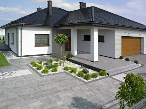 Nowoczesny dom z podjazdem i chodnikiem wykonanymi z różnych rodzajów kostki brukowej, tworzących harmonijną całość.
