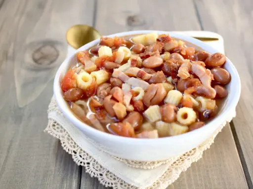 Una ciotola di pasta e fagioli in scatola, con pomodoro e pancetta, servita su un tovagliolo di pizzo.