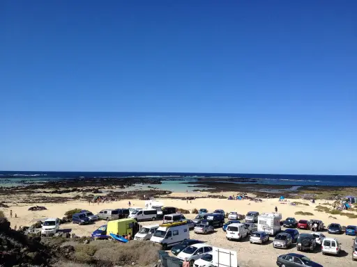 Día soleado en Lanzarote con niños. Coches aparcados en la playa, familias disfrutando del mar y la arena.