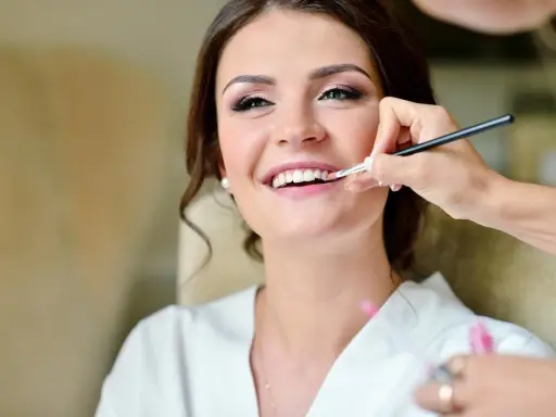 Maquillaje para madrina de boda: una mujer sonríe mientras le aplican brillo labial.
