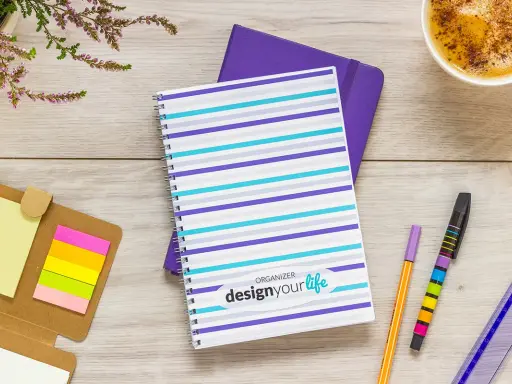 Pomysł na kalendarz: kolorowy notatnik z napisem "design your life", obok długopisy, karteczki i kawa.
