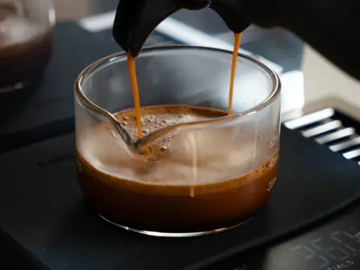 Frisch gebrühter Espresso fließt in ein Glasgefäß, die goldbraune crema de cafe bildet eine samtige Schicht.