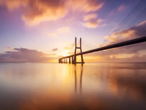 Ponte sospeso sull'acqua calma, con un cielo colorato da un tramonto mozzafiato. Una foto da fare al tramonto, perfetta per catturare la magia del momento.
