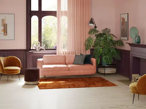 Przytulny salon z sofą w kolorze pudrowy róż, aksamitnym fotelem i dywanem w odcieniu miedzi.