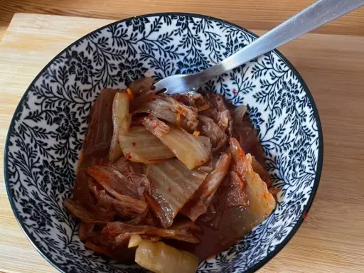 Miseczka z domowym kimchi, widelcem, na drewnianej desce.