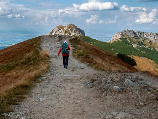 Szlak na czerwone wierchy z Kuźnic. Turystka z plecakiem idzie kamienistą ścieżką wśród traw.