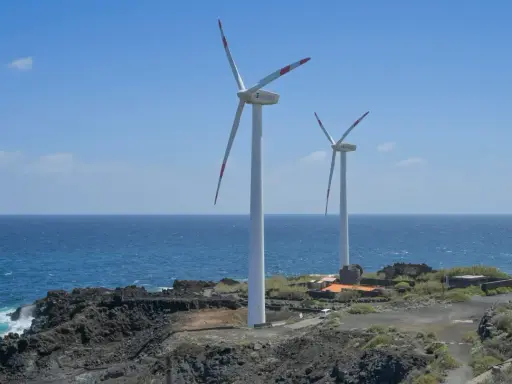 Zwei Windräder stehen an einer felsigen Küste Spaniens. Sie sind Teil des Strommixes und erzeugen saubere Energie.