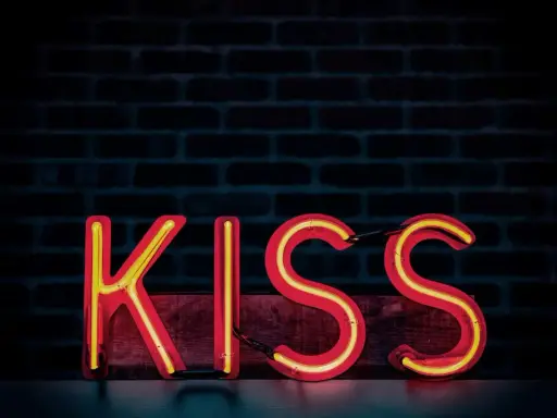 Neonowy napis KISS na tle ceglanej ściany. Zasada KISS: Keep It Simple, Stupid.