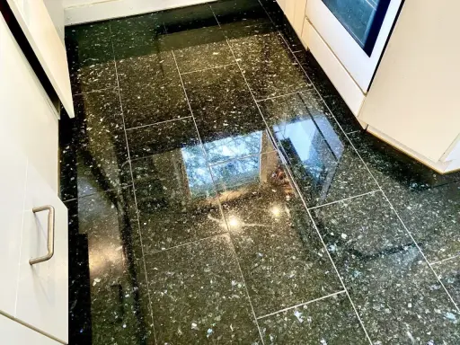 Glänzender Granitboden, der nach dem Granit reinigen strahlt. Spiegelungen von Fenstern und Lichtern auf den dunklen Fliesen.