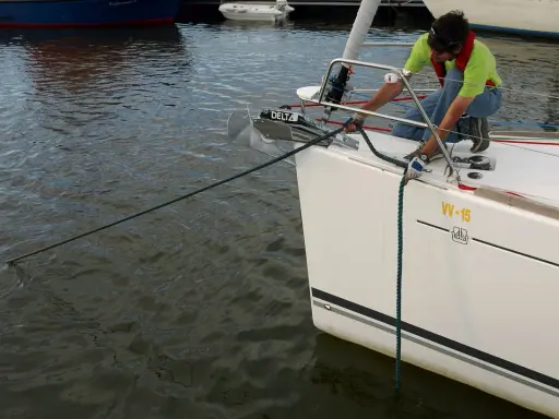 Un homme en gilet de sauvetage ajuste la pendille du bateau, une corde verte s'étendant sur l'eau calme.