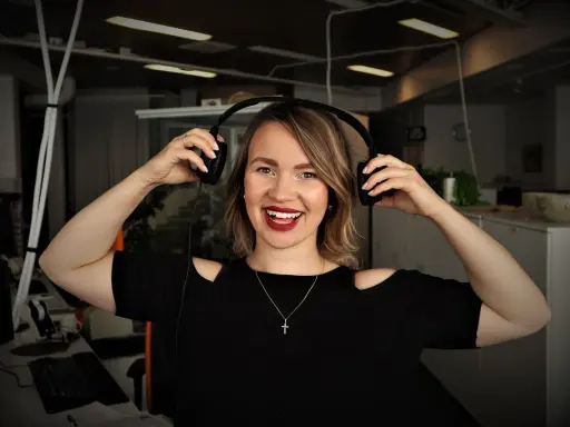Uśmiechnięta kobieta z słuchawkami na uszach, słucha podcastów do nauki angielskiego.