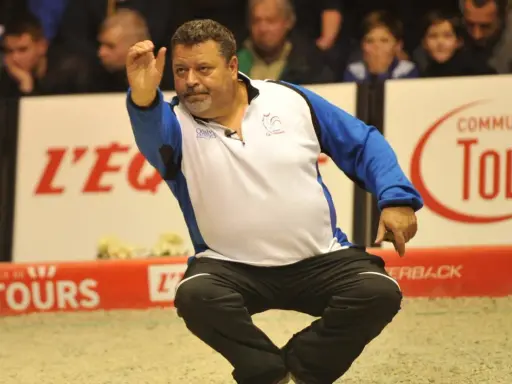 Un joueur de pétanque français connu, en pleine action, lance sa boule.