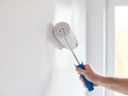 Mano con rodillo pintando una pared blanca, renovando el hogar.