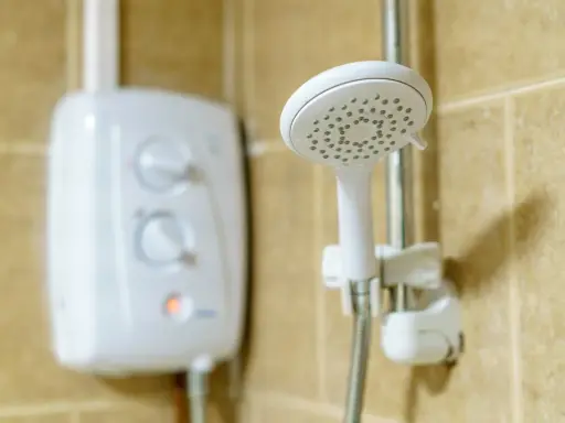 Ein weißer Boiler für die Dusche mit Reglern und eine Duschbrause an der Wand.