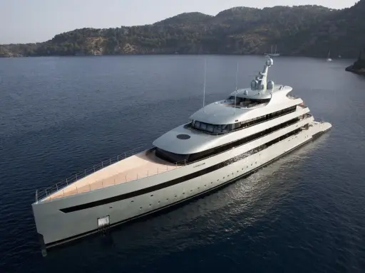 Un yacht de luxe gris clair navigue dans une baie. Le choix couleur coque bateau est élégant, contrastant avec le bleu profond de l'eau.