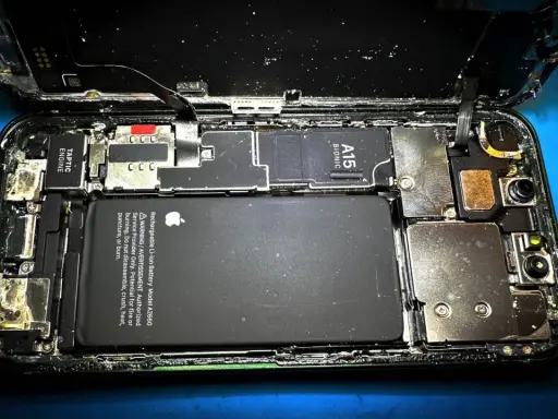Rozkręcony iPhone z widoczną baterią i procesorem A15 Bionic. Wygląda na to, że ten zalany iPhone wymaga pilnej naprawy.