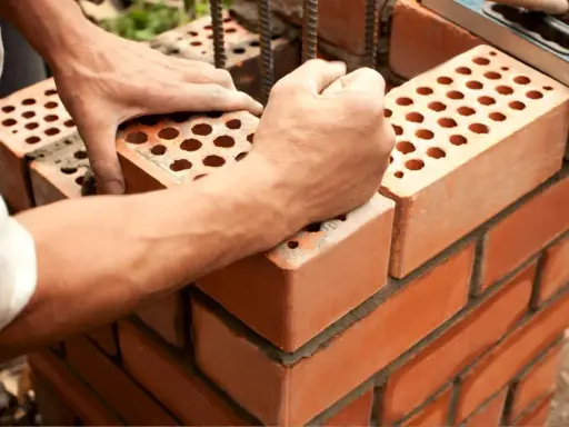 Manos colocan ladrillo con huecos, mostrando sus dimensiones. Construcción de pared con mortero.