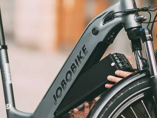 Ręce wyjmujące czarną baterię z ramy roweru elektrycznego JOBORBIKE.