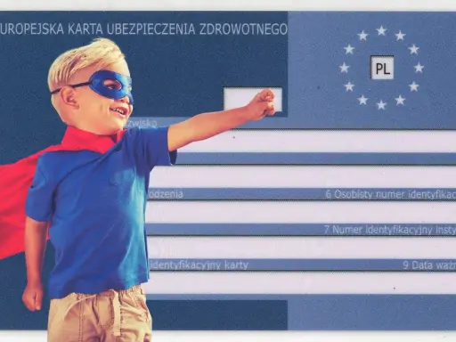 Mały superbohater z czerwoną peleryną i niebieską maską pozuje na tle karty EKUZ dla dziecka.